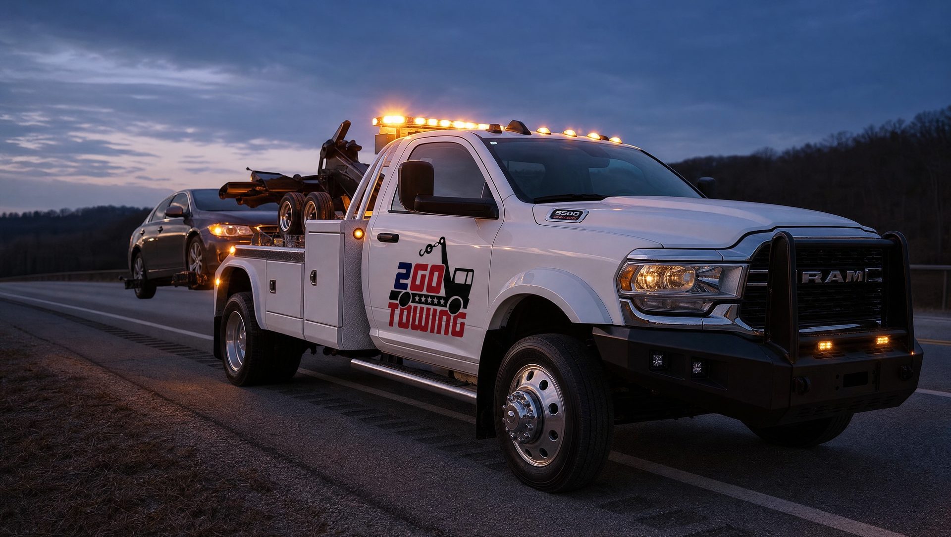 Auto Towing 2Go tow truck towing a car on the highway shoulder at dusk